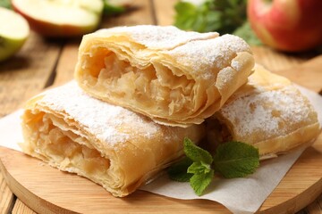 Pieces of tasty apple strudel with powdered sugar and mint on wooden table, closeup