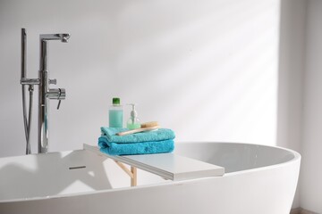 White board with soft towels, brush and cosmetic products on tub indoors