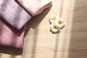 Soft towels and plumeria flowers on wooden table, flat lay