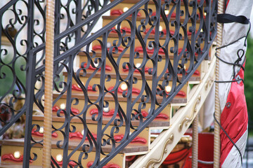 Close-up of ornate staircase with wrought iron railing and lights on a traditional vintage carousel or fairground ride.