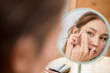 Young beautiful Asian woman checking her facial skin in mirror feeling worried about freckles...