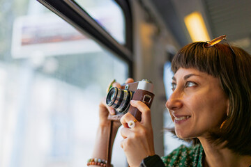 girl riding a train and taking pictures. film camera. stylish girl with a camera in her hands sits...