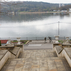 Stone staircase leading to lakeside promenade with statues and overcast sky