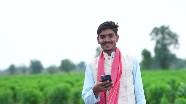 young indian farmer holding smartphone standing in agriculture field	
