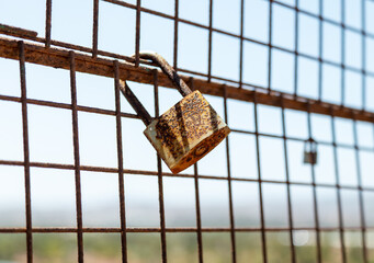 A rusty padlock on a weathered metal fence—likely placed as a sentimental symbol. In the...