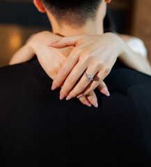 The bride gently hugs the groom by the neck close up. The hands of a woman with a wedding ring on...