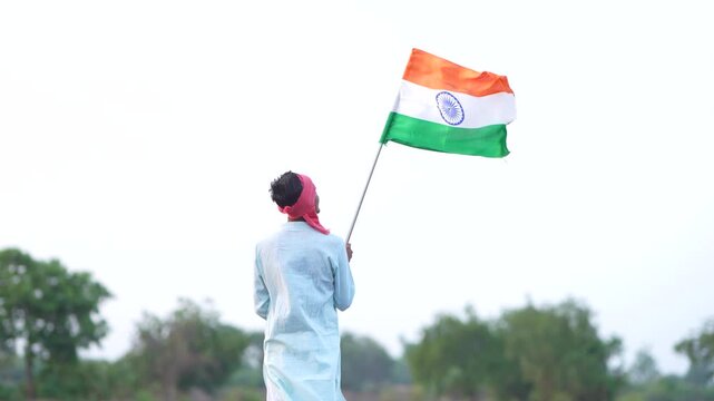 Young indian farmer waving indian flag at agriculture field 