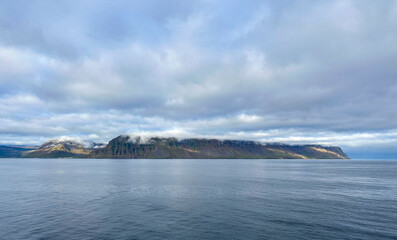 A view of Iceland from the water with clouds touching the top of the land