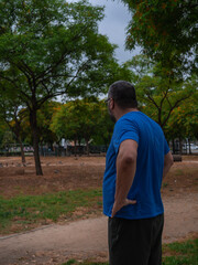 a man with short hair and a beard, wearing a blue t-shirt and dark pants, standing outdoors in a...