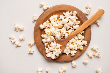 White salty or sweet popcorn in wooden bowl and a spoon on light gray background, top view flat lay. Corn flakes, food for movie or cinema. Delicious appetizer, party snack. Empty space for text