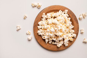 White salty or sweet popcorn in wooden bowl on light gray background, top view flat lay. Corn flakes, food for movie or cinema. Delicious appetizer, party snack. Empty space for text