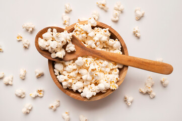 White salty or sweet popcorn in wooden bowl and a spoon on light gray background, top view flat lay. Corn flakes, food for movie or cinema. Delicious appetizer, party snack. Empty space for text