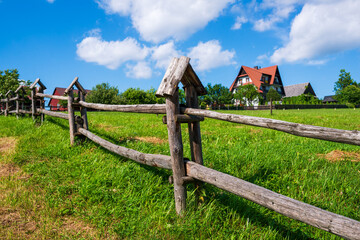 Traditional wooden fence with pointed tops stretches across a green lawn, with village houses and...