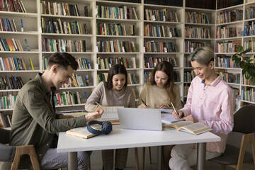 Collaborative research and note taking. Busy young diverse students zoomers gather around table in classroom focused on writing up information using paper online literature prepare academic assignment
