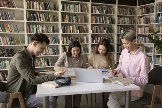Collaborative research and note taking. Busy young diverse students zoomers gather around table in classroom focused on writing up information using paper online literature prepare academic assignment