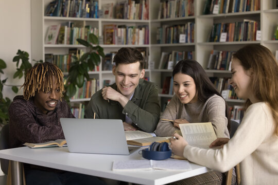 Blended education and peer learning. Multiethnic diverse gen z students pupils use notebook in library watch web based video lesson together prepare group project reviewing online lecture paper books
