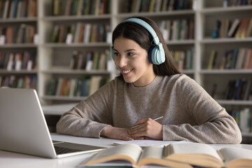 Digital learner. Interested smiling teen girl remote learning student wear wireless headphones...