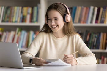 Modern day education. Smiling teen girl college student wearing wireless earphones learning on...