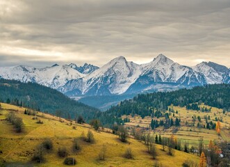 Tatras village in the autumn mountain valley. Autumn mountain village, with a beautiful autumn sun, snowy mountain peaks in the background. Mountain village in autumn landscape.