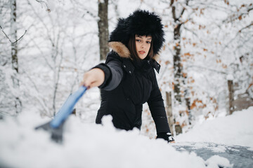 A woman is clearing snow from the car