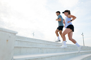 Two individuals engage in a spirited workout session as they jog up outdoor steps in a bright, open...