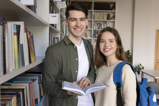 Reading generation. Portrait smart successful diverse student couple stand at bookstore or campus library smile at camera hold paper book reflect motivation to gain knowledge share academic enthusiasm
