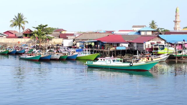Traditional fishing activities using wooden boats on the Manggar River with a background of a row of boats anchored in the fishing village in the afternoon