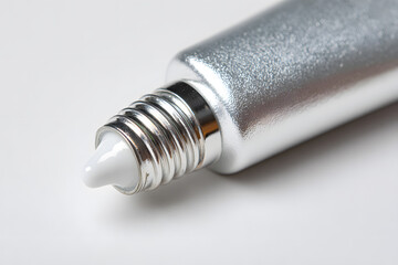 Silver tube with white cream tip is poised on a clean surface, perfect for skincare or cosmetic applications