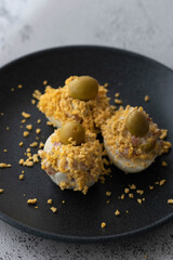 huevos rellenos con mayonesa, jamón aceitunas verdes y yema molida sobre un plato negro, con fondo...
