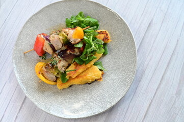 Top-down view of a colorful plated meal featuring a grilled chicken skewer, fresh salad, and creamy...