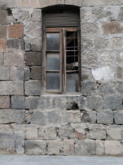 This weathered stone wall features an old wooden window, hinting at years of history. The rough texture and faded colors tell stories of time. Can be used as elements for design projects. 