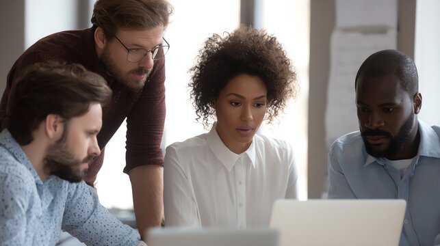 Four diverse colleagues focused and collaborating around a laptop in a bright modern office.