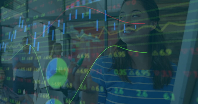 Gesturing woman in striped top presenting market data at open-plan office with stock charts overlay