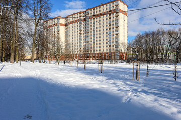 Modern residential apartment building and snowy city park with bare trees in winter