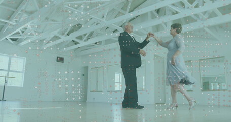 Dancing senior couple wearing suit and blue dress in dance studio, with hardwood floor and mirrors