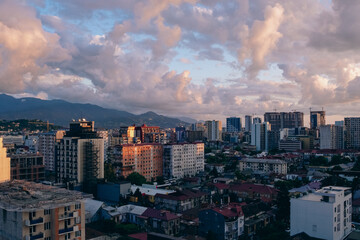 Fototapeta premium Batumi skyline with diverse architecture, dramatic clouds, and mountain backdrop at sunset. Georgia urban view with old and new buildings.