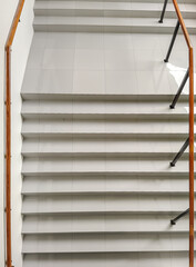 A high-angle view looking down a modern minimalist staircase with gray tiled steps and a wooden handrail.