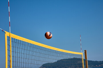 Volleyball in the air over a yellow net during a beach match in Baiona under a clear blue sky