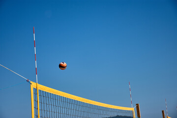 Volleyball in the air over a yellow net during a beach match in Baiona under a clear blue sky