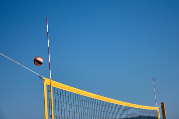 Volleyball in the air over a yellow net during a beach match in Baiona under a clear blue sky
