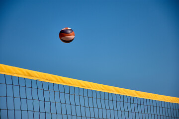 Volleyball in the air over a yellow net during a beach match in Baiona under a clear blue sky