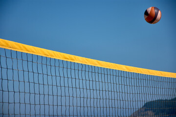 Volleyball in the air over a yellow net during a beach match in Baiona under a clear blue sky