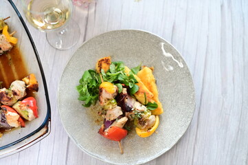 Top-down view of a colorful plated meal featuring a grilled chicken skewer, fresh salad, and creamy polenta on a white background.