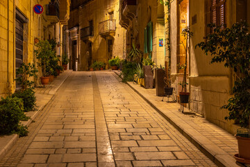 Charming narrow street in Birgu lit by warm evening lights, Malta.