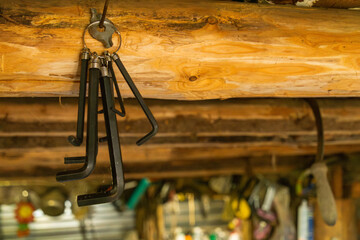 Set of black hex keys hanging from a keyring on wooden beams in a workshop, surrounded by various...