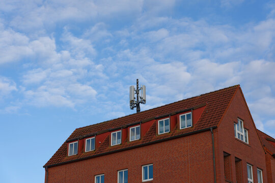 Red brick apartment building with roof antenna Broadcasting UMTS LTE WLAN 5G 6G Mobile Data - Powered by Adobe