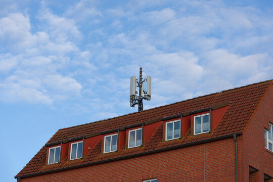 Red brick apartment building with roof antenna Broadcasting UMTS LTE WLAN 5G 6G Mobile Data - Powered by Adobe