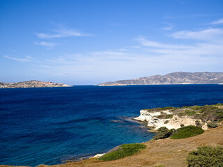 Scenic coastal view on Milos island, Greece — deep blue sea meets arid landscape beneath a sky with soft clouds, evoking calm Mediterranean beauty.