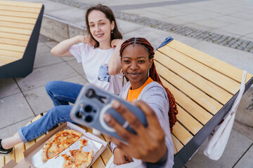 Young women smiling and posing for selfie with pizza