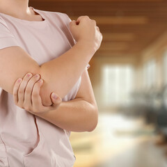 Elbow pain and injury – hands holding painful arm, fitness area background. Sport workout,...